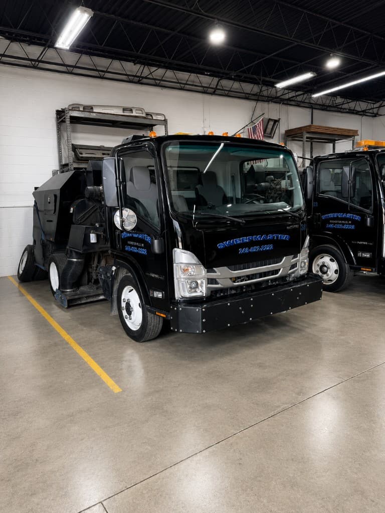 Front view of a black Sweepmaster Isuzu sweeper truck